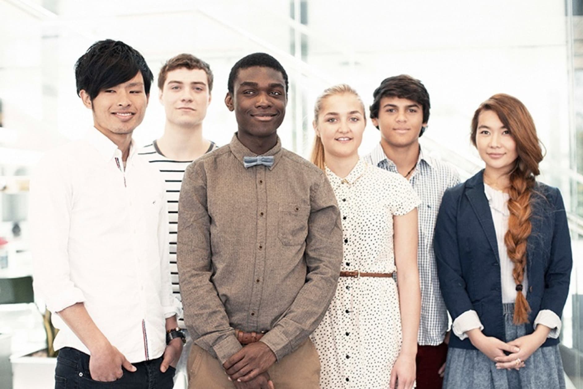 A group of six young adults, three males and three females, pose for a photo. They are standing close together and smiling at the camera.