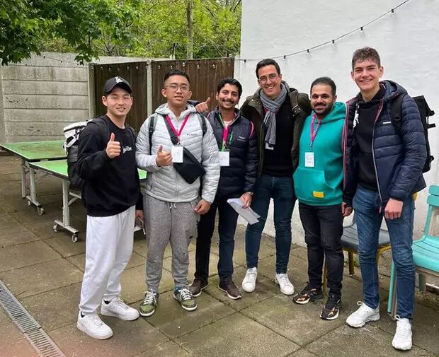 A group of seven young men are posing for a photo outdoors. They are all smiling and appear to be in good spirits, possibly at an event or gathering.