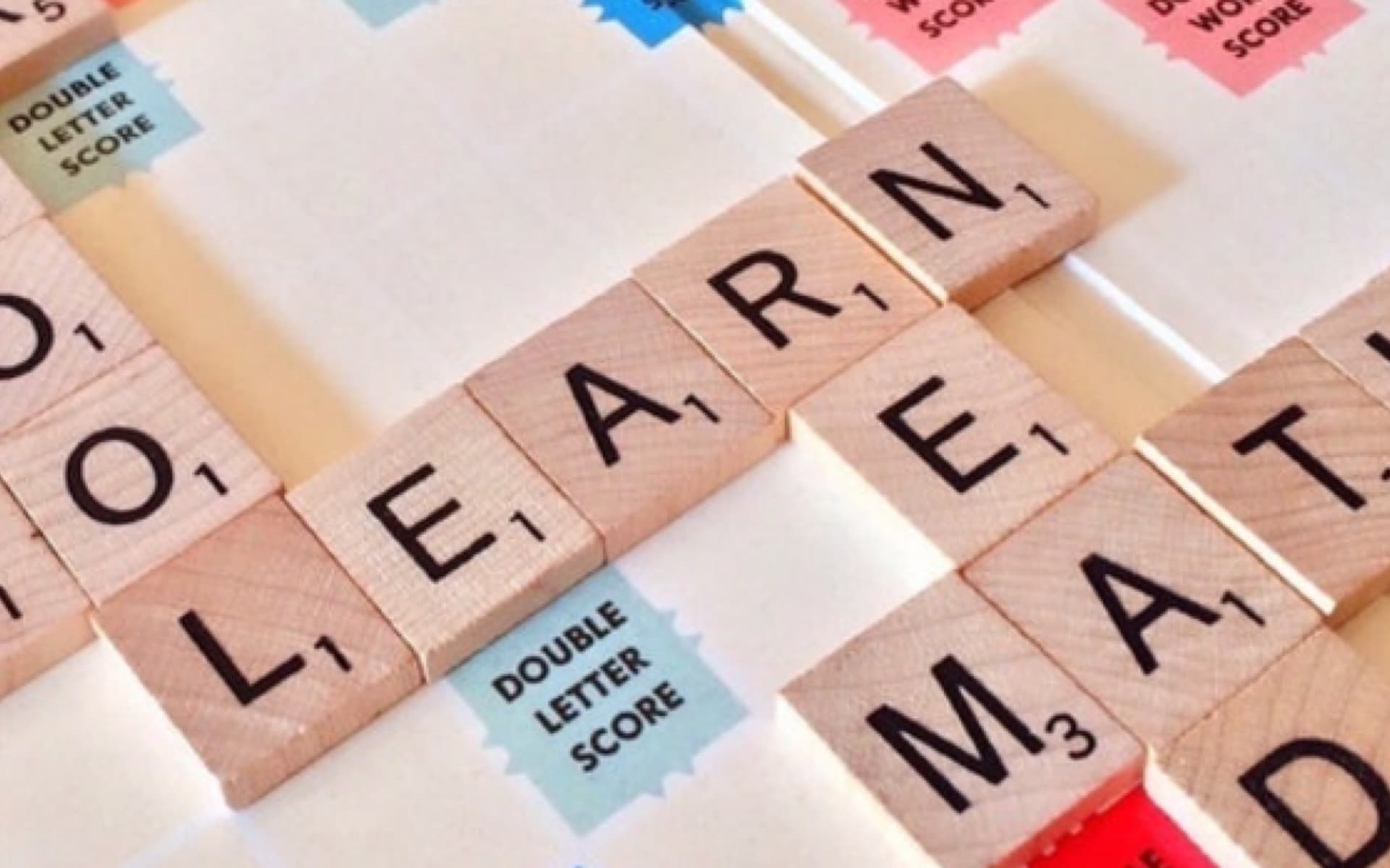 This image displays a Scrabble game board featuring the words "LEARN" and "MATH" spelled out with wooden letter tiles, highlighting the connection between education and mathematics.