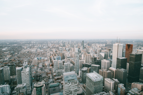 This is a high-angle aerial view of a sprawling cityscape, featuring numerous skyscrapers and buildings stretching towards the horizon under an overcast sky.