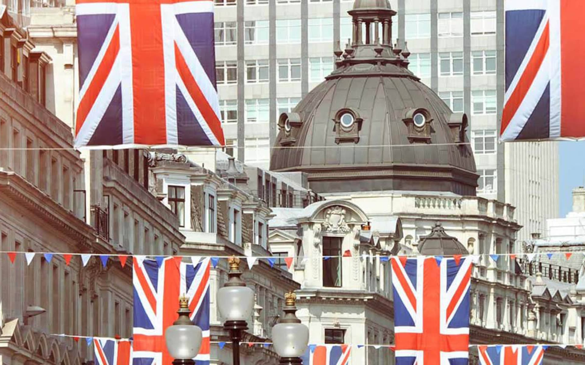 This image captures a London street adorned with Union Jack flags and bunting, suggesting a festive occasion. Historic architecture and a modern office building form the backdrop.