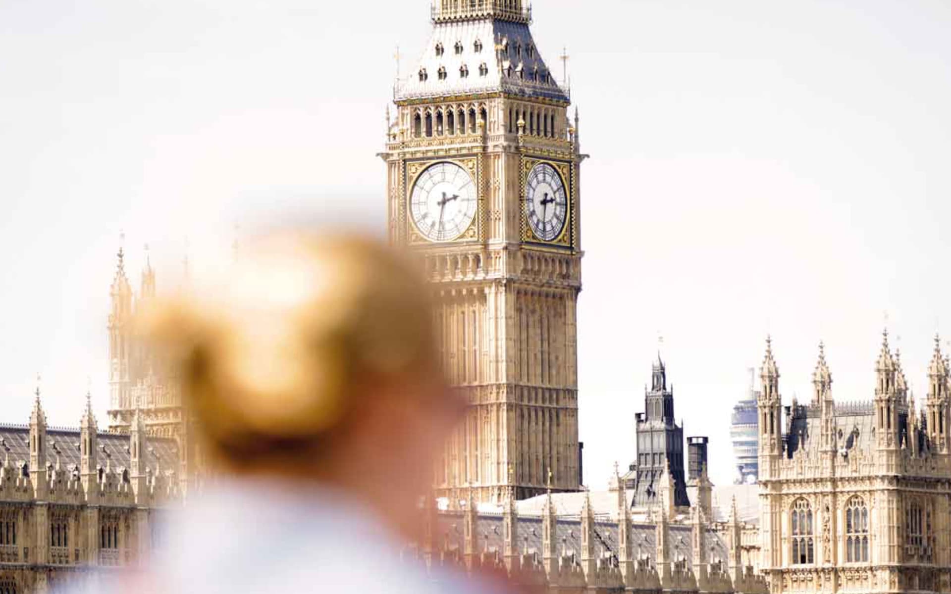The image features the Big Ben clock tower in London, with the Palace of Westminster visible in the background. An out-of-focus person is in the foreground.