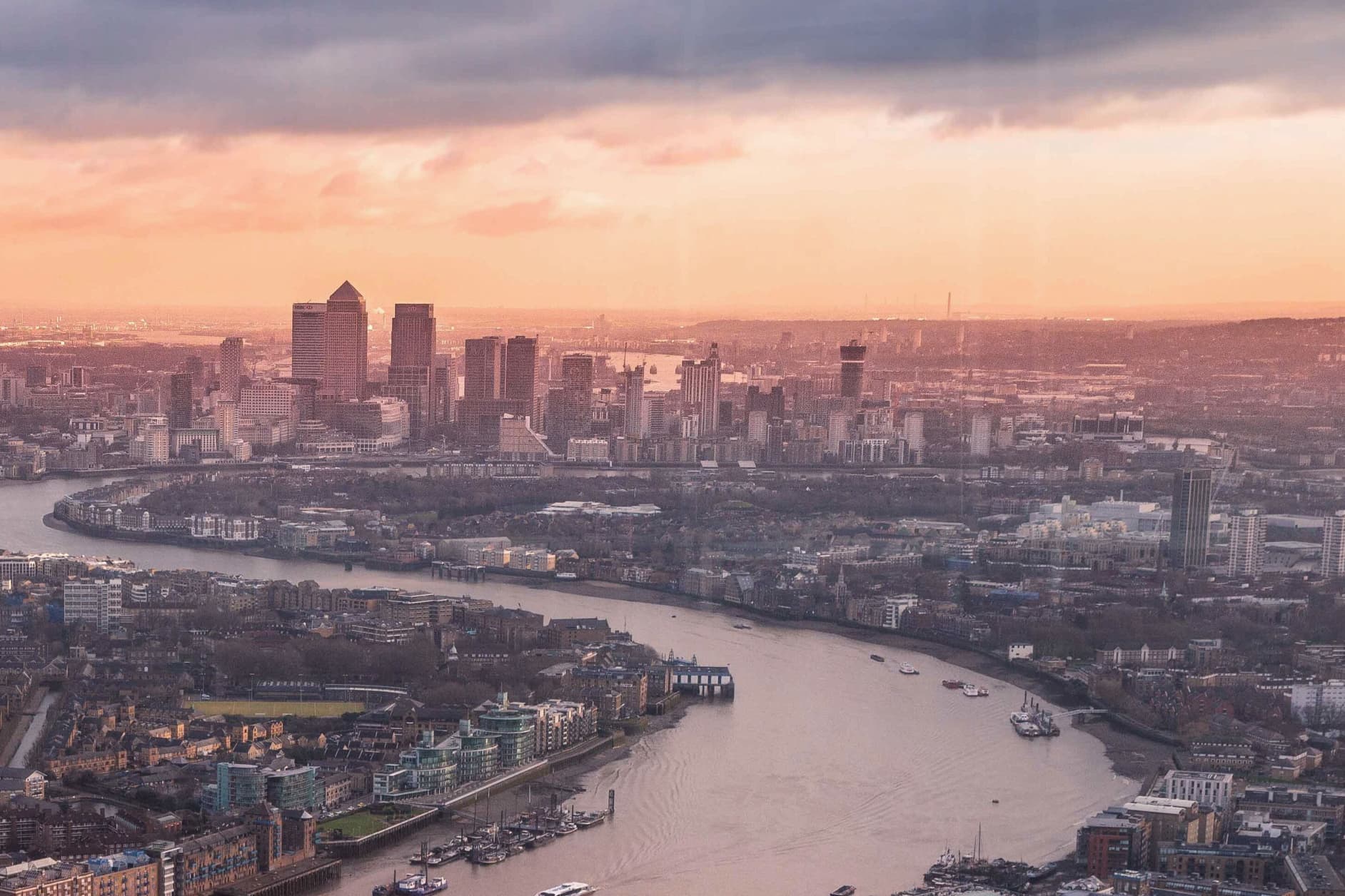 A picturesque view of the London skyline at sunset, with the River Thames winding through the city, blending modern buildings with the clouds.