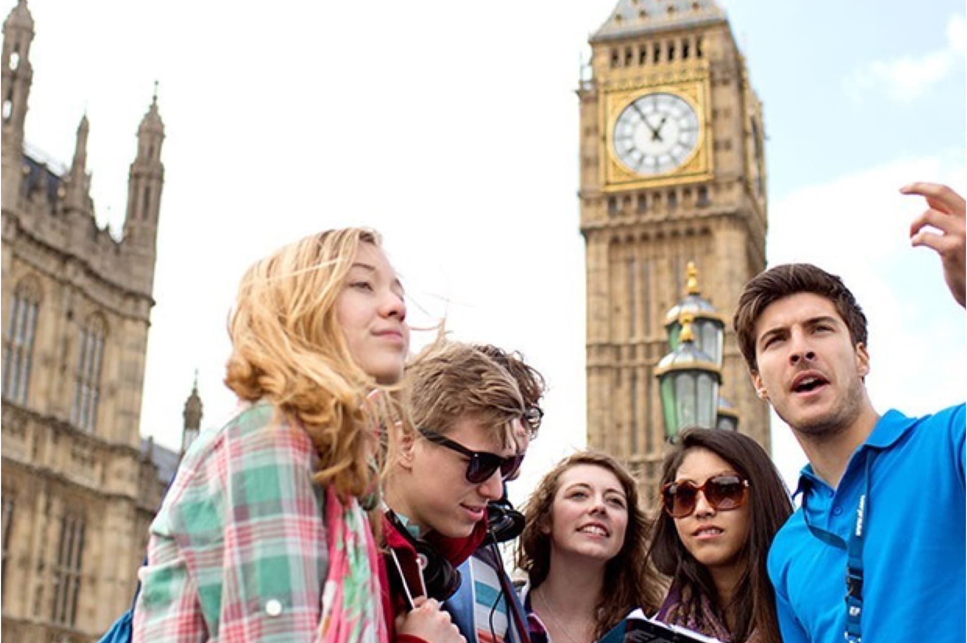 A group of five young tourists are gathered in front of the iconic Big Ben clock tower in London, looking around with curiosity and interest.