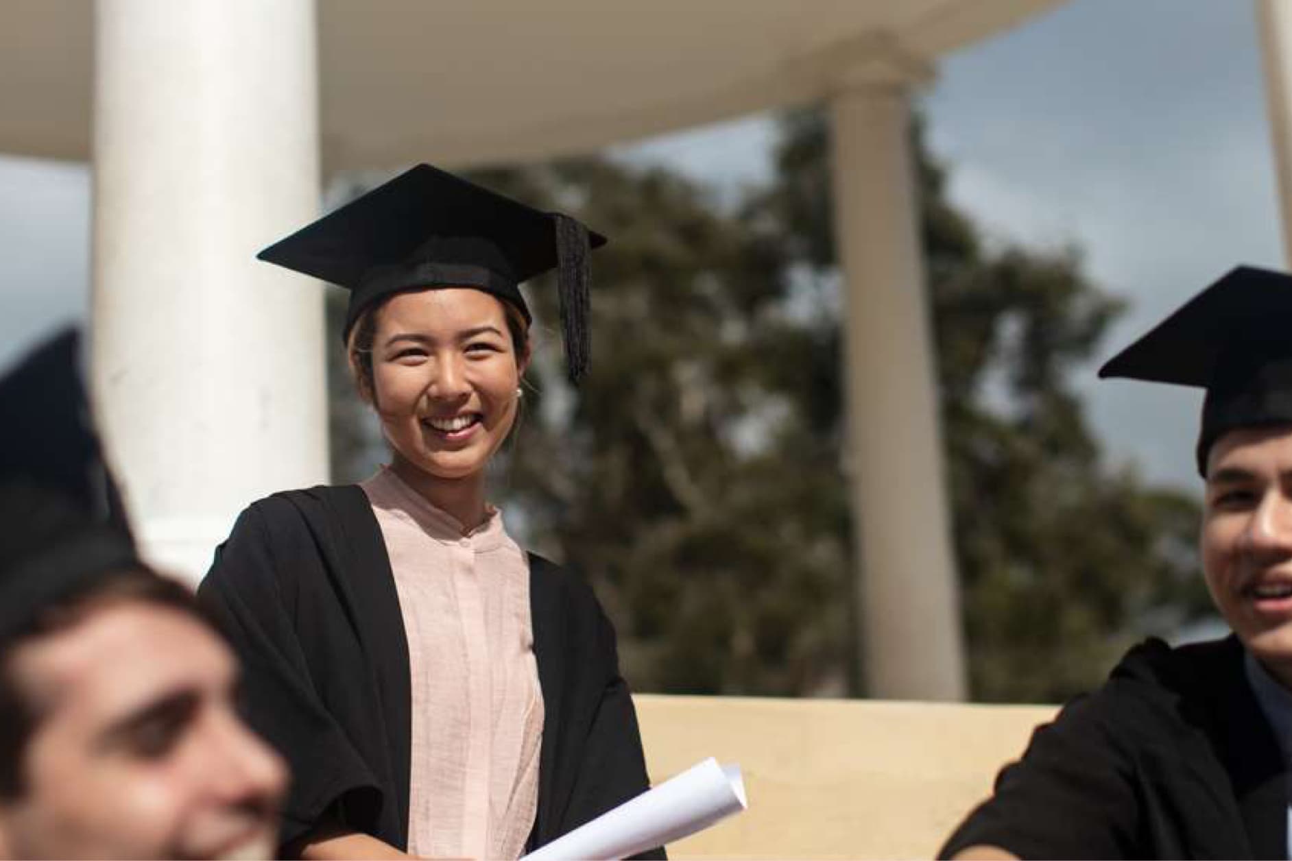 Several graduates, dressed in traditional graduation gowns and caps, are smiling at the camera while holding their diplomas.