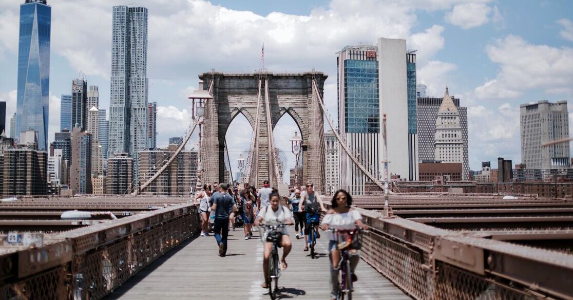 The Brooklyn Bridge in New York City is bustling with pedestrians and cyclists, crossing with the city skyline in the background.