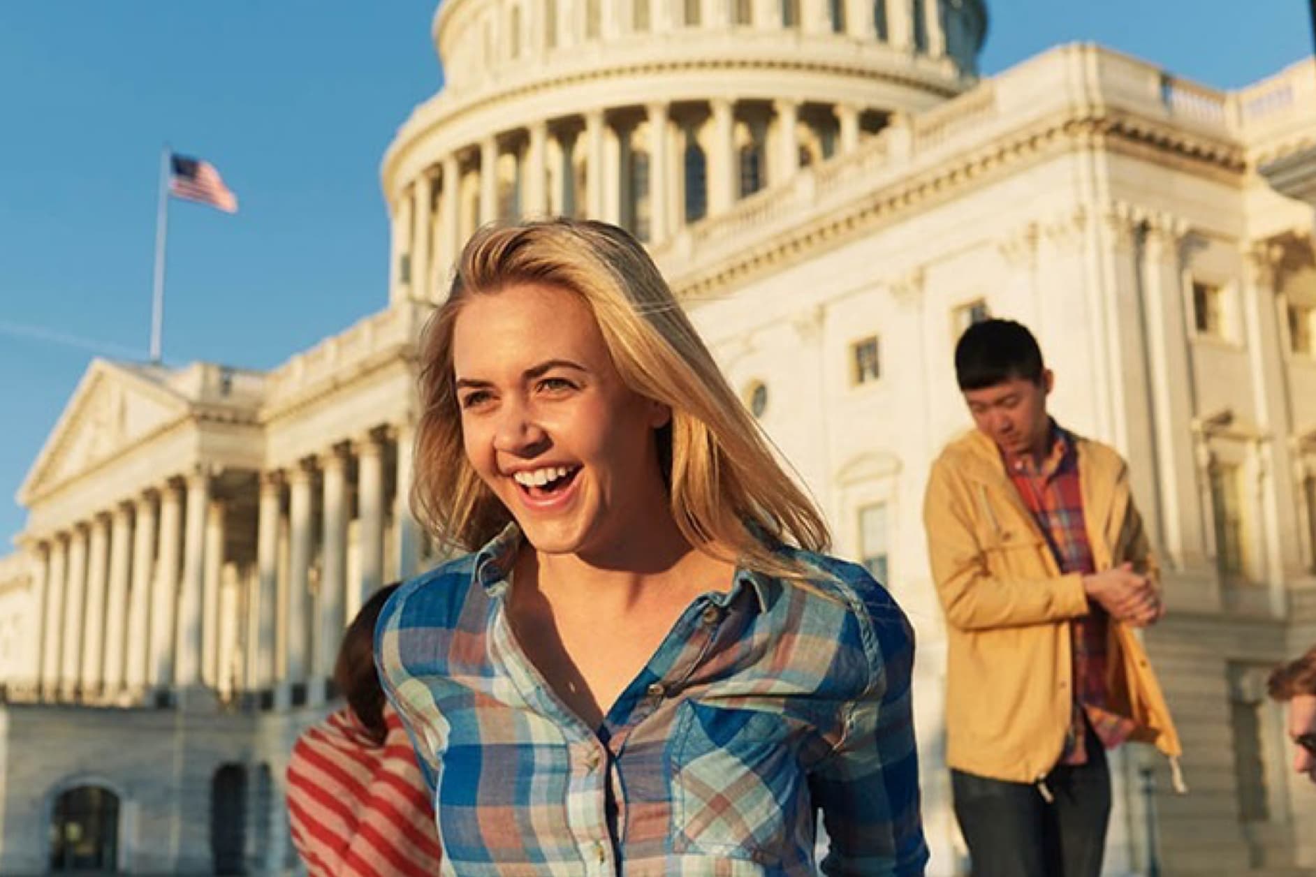 A group of young adults are smiling and laughing while standing in front of the United States Capitol Building on a sunny day.