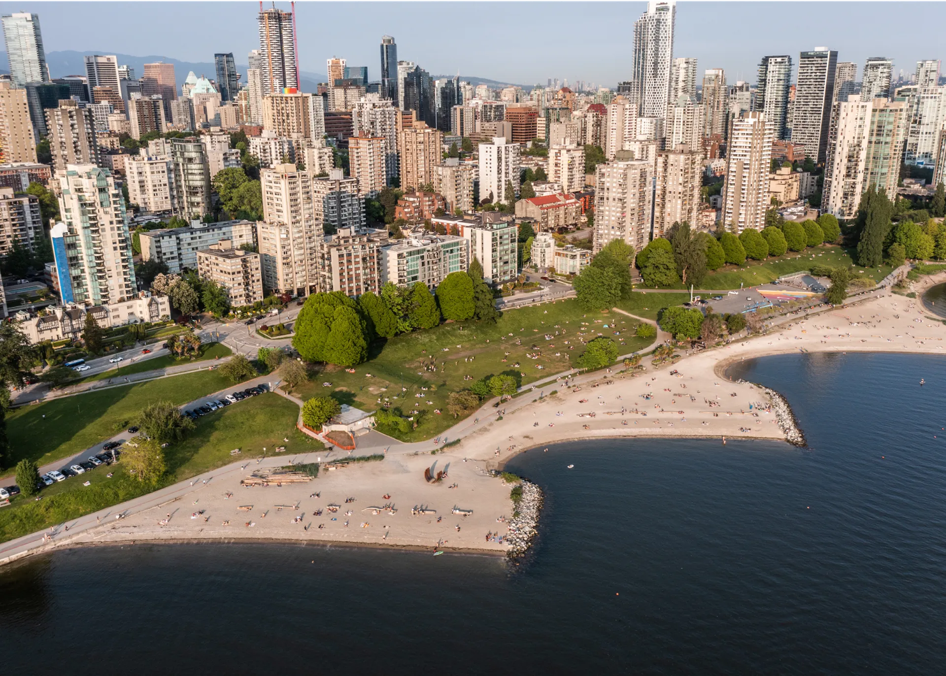 This is an aerial view of a crowded beach with a cityscape in the background. People are sunbathing and relaxing on the sand, while others are enjoying the water.