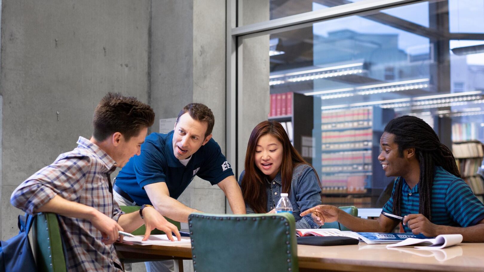 Four students are gathered around a table, actively engaged in a study session. They appear to be collaborating on a project, with books and papers spread out before them.