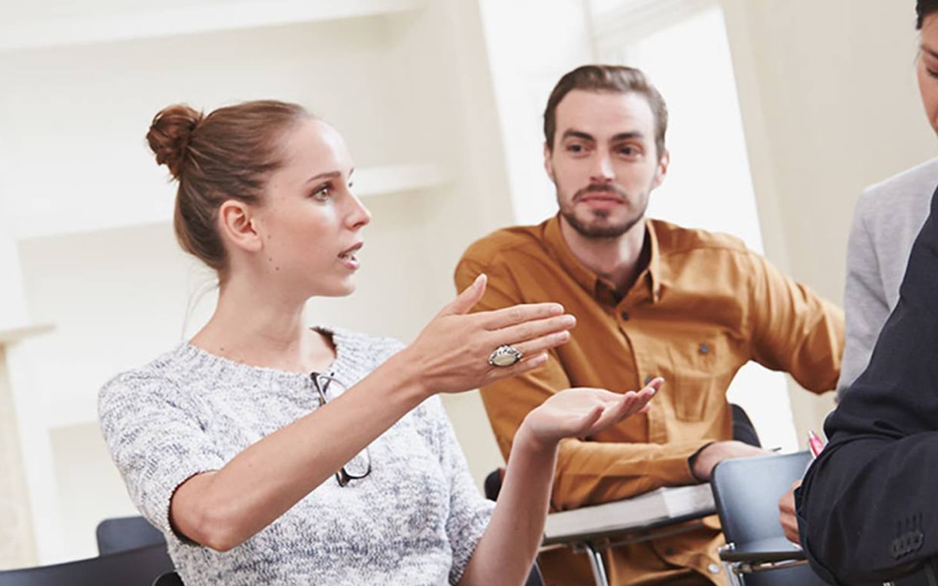 A woman is explaining something with hand gestures while a man attentively listens to her. They appear to be in a meeting or seminar setting.