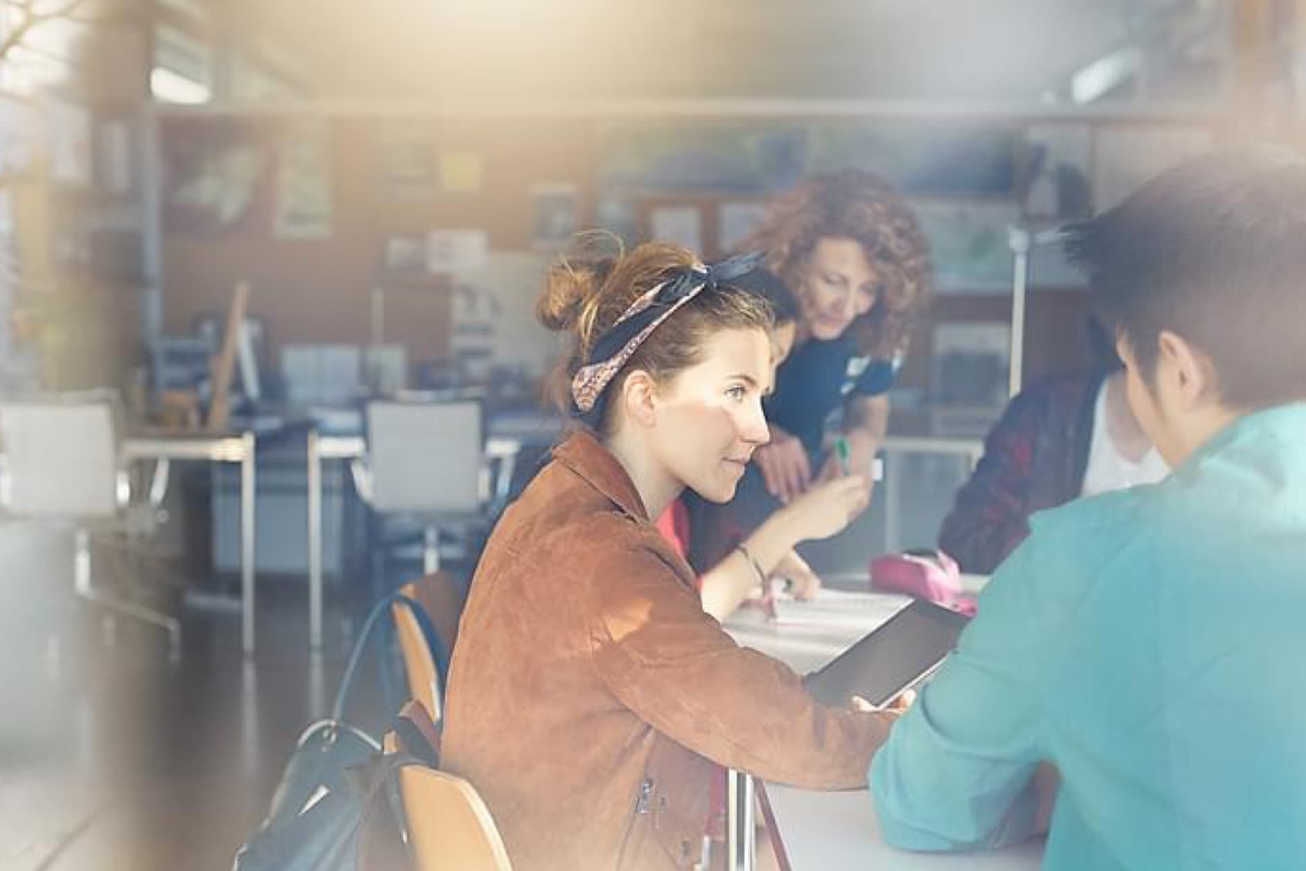 Three young women collaborate on a project in a bright, modern learning space, with one pointing at a tablet.
