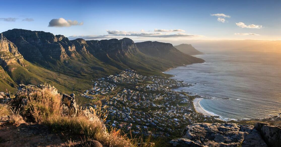 A breathtaking view of Cape Town, South Africa, with the majestic mountains overlooking the city and the ocean as the sun sets.